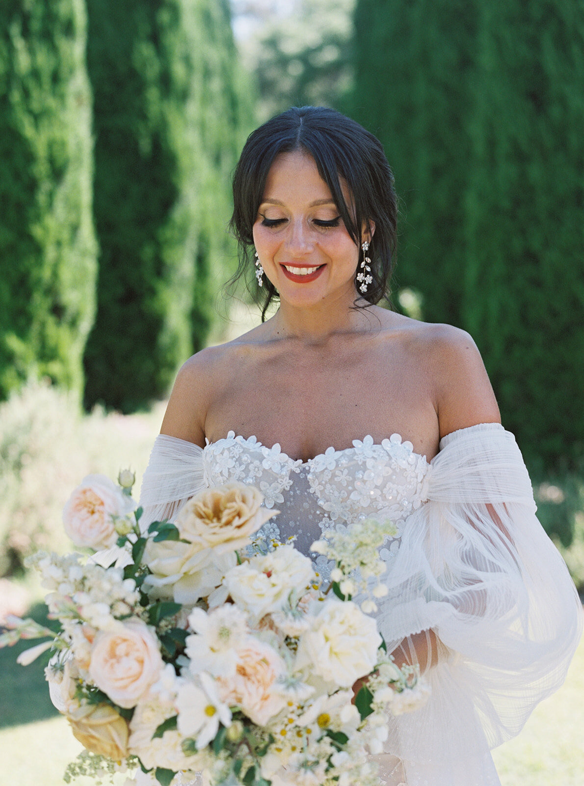 A bride in an off-the-shoulder gown holding a bouquet of cream and peach roses