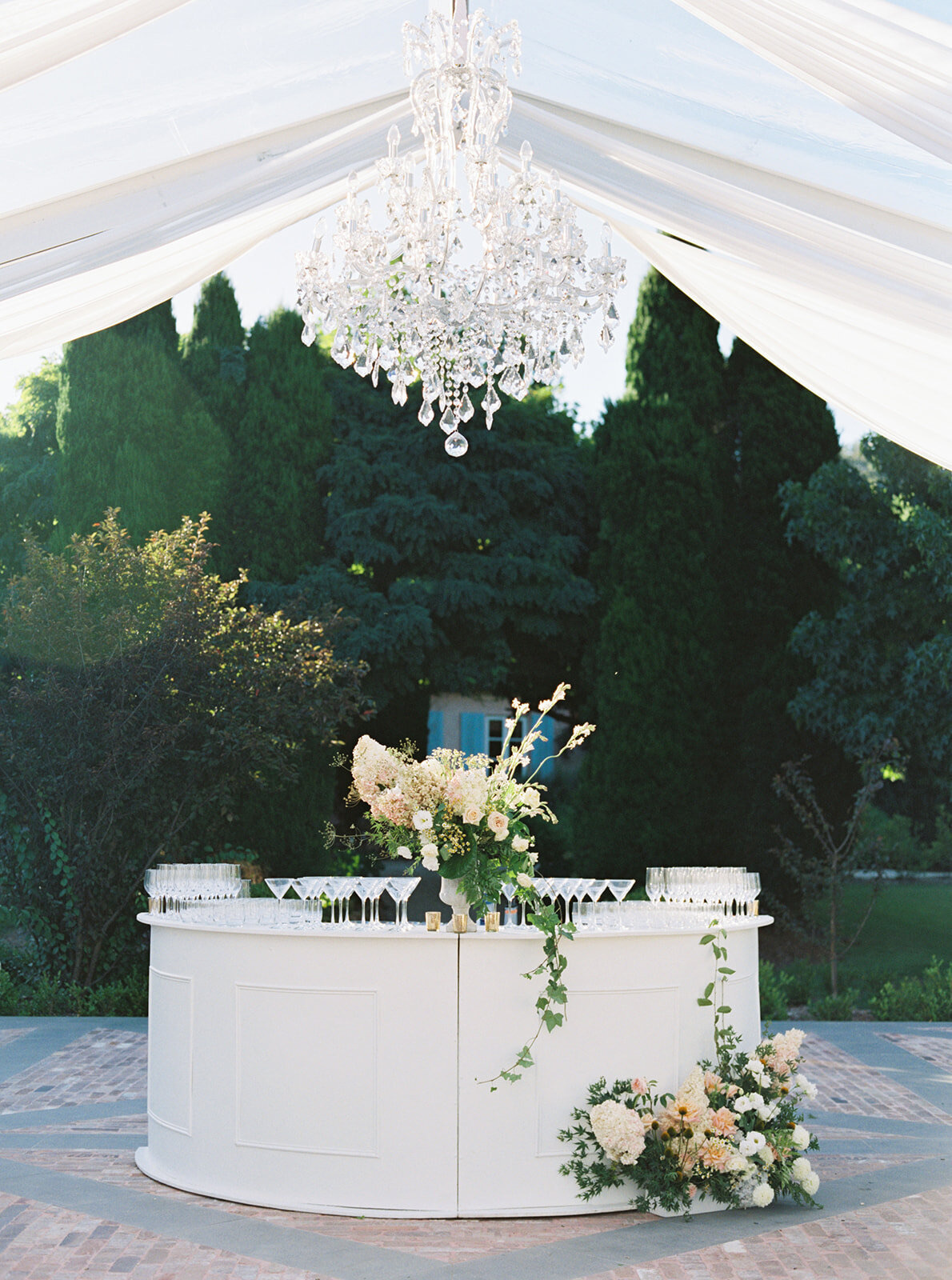 A white bar under a crystal chandelier hung from draped fabric outdoors