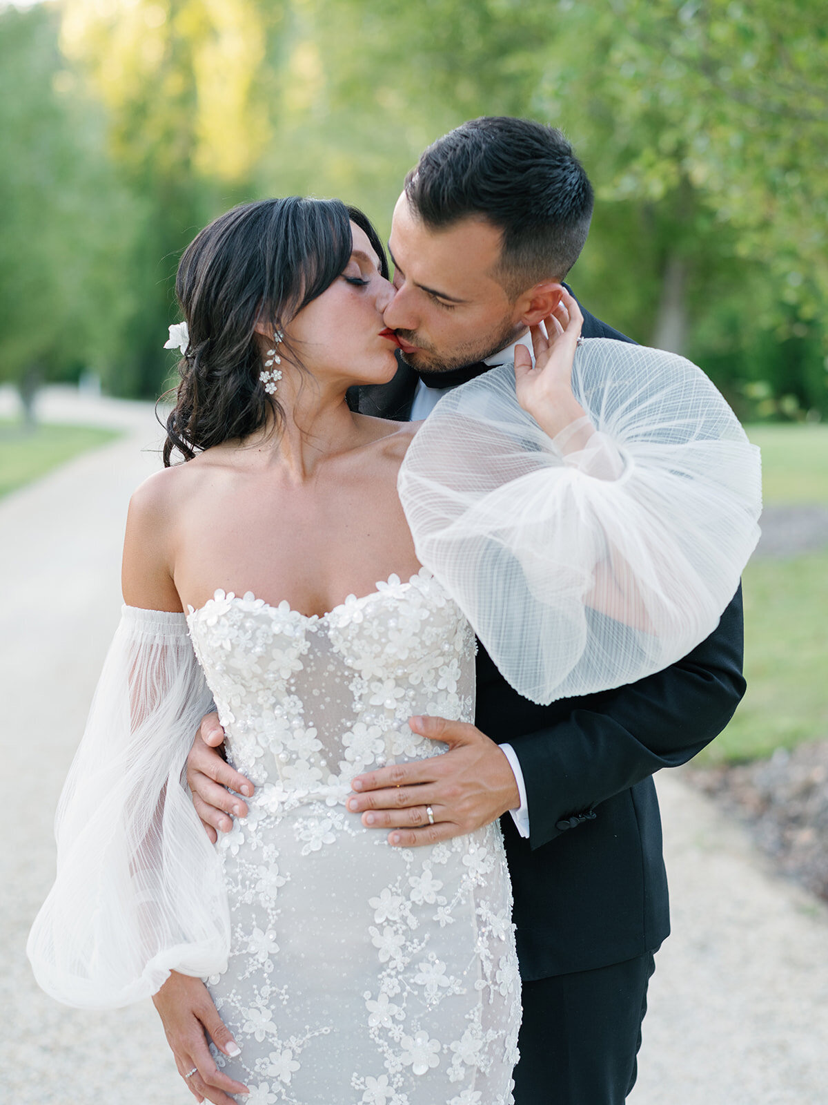 A groom kissing his bride's cheek on a garden path