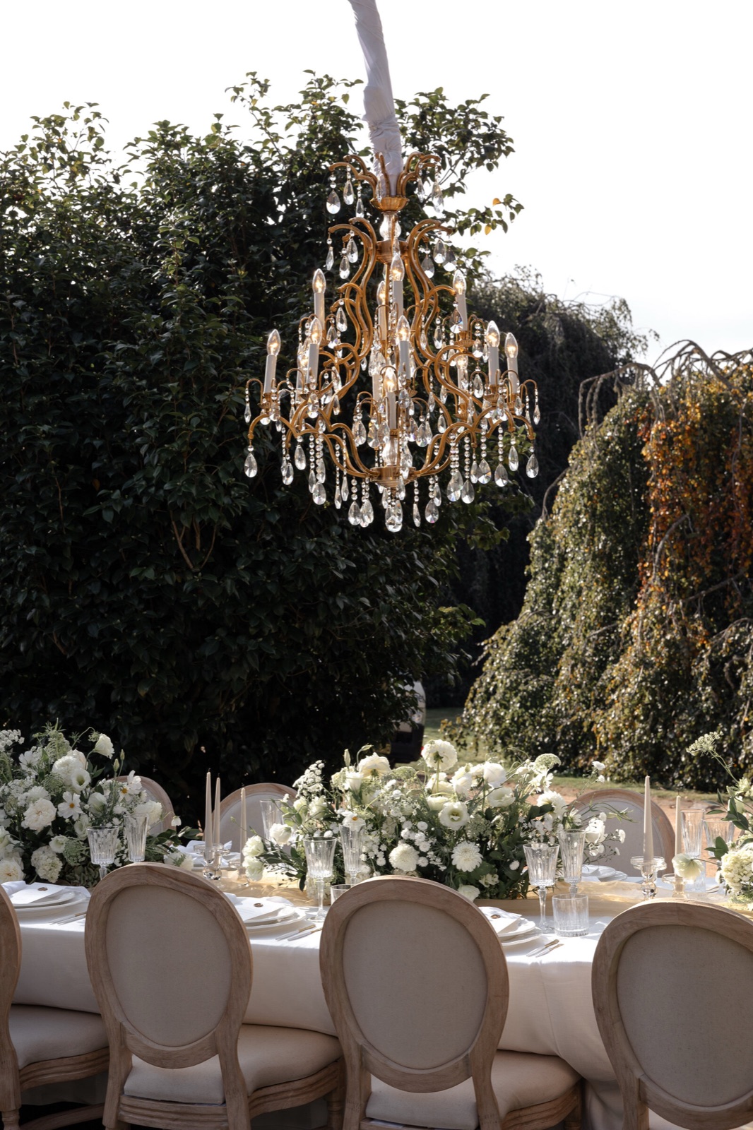 A long reception table under chandeliers in a garden