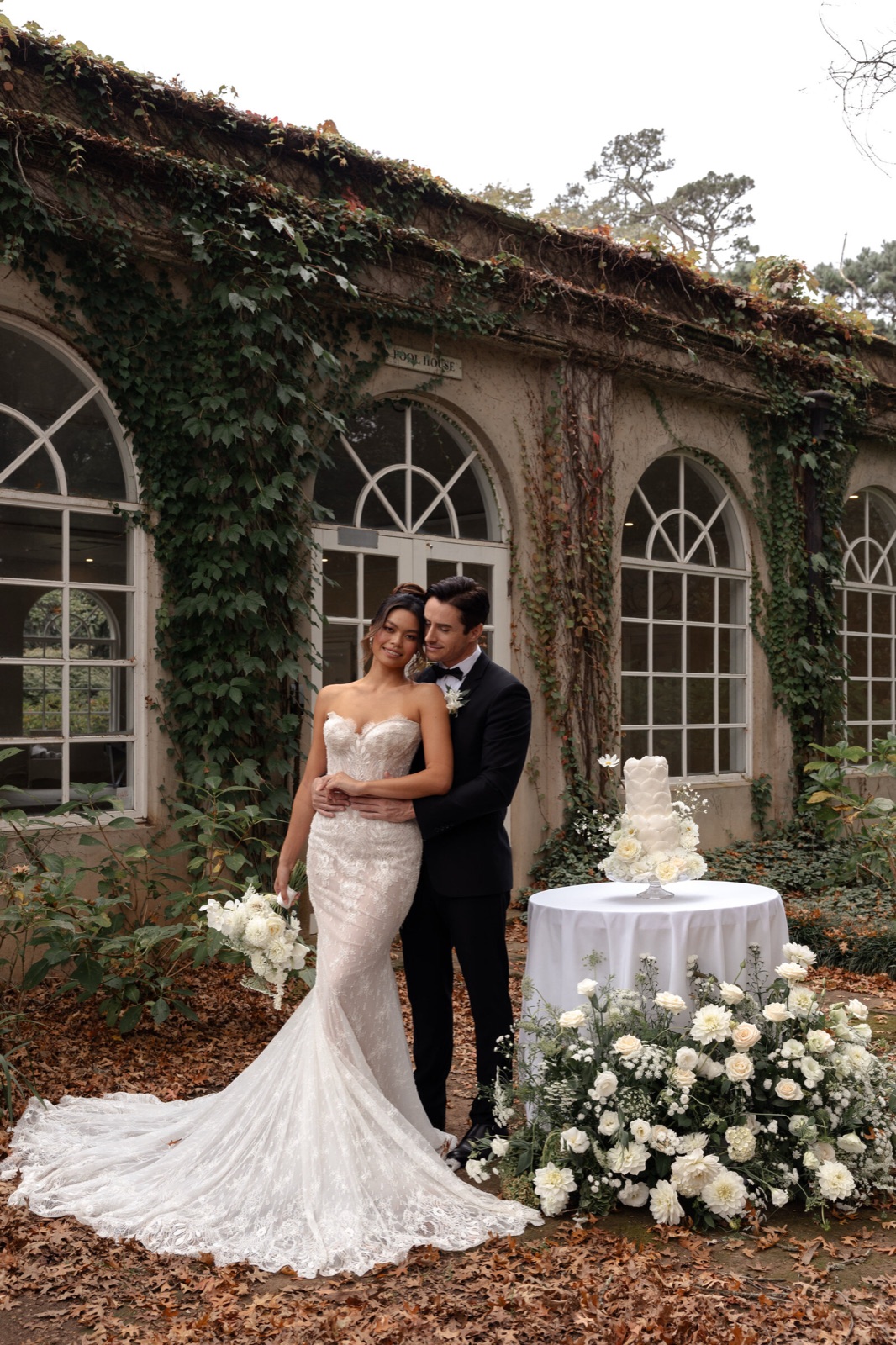 A couple beside their cake table in front of an ivy-covered orangery